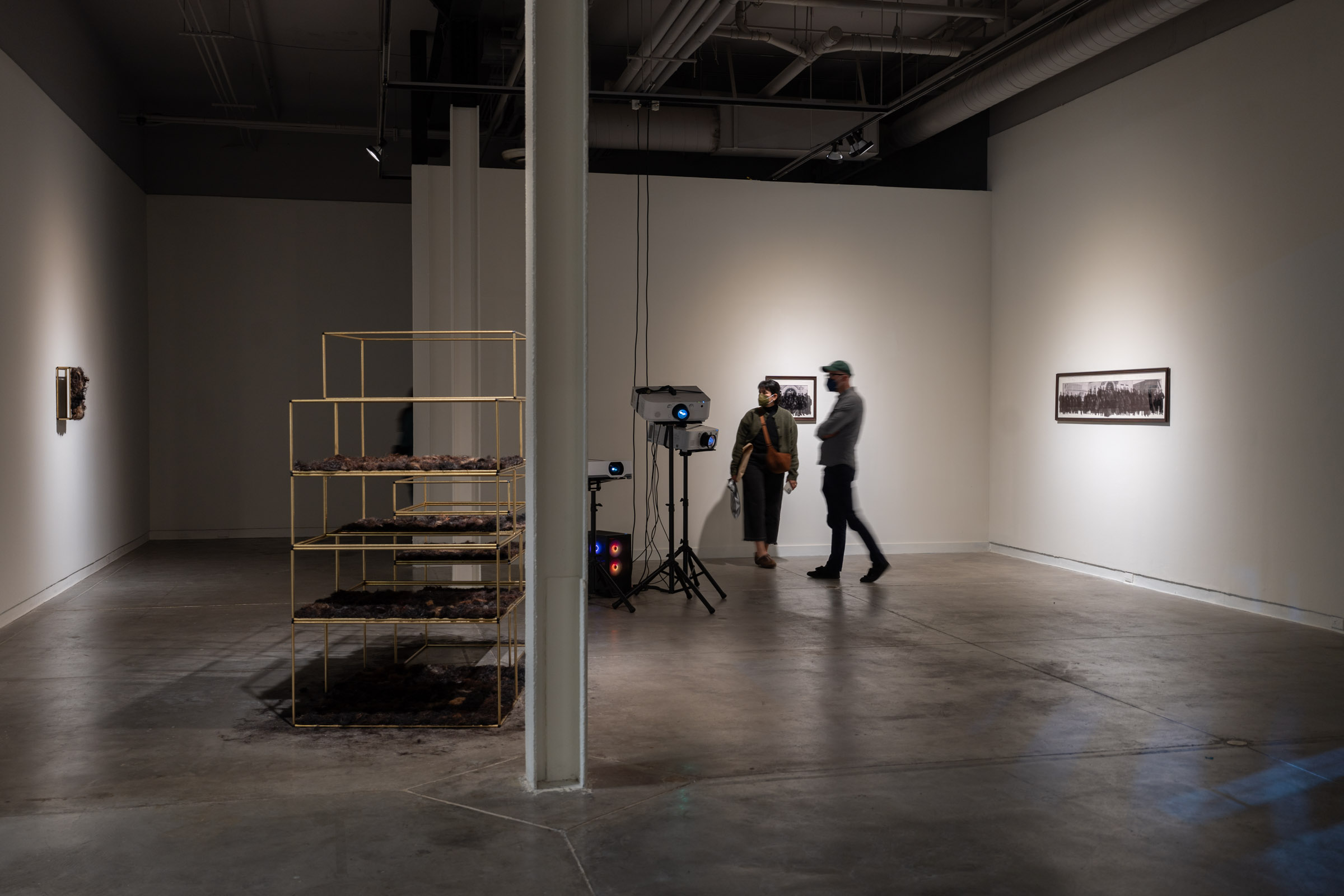 Visitors navigating the exhibition with projector and sculptural structures visible